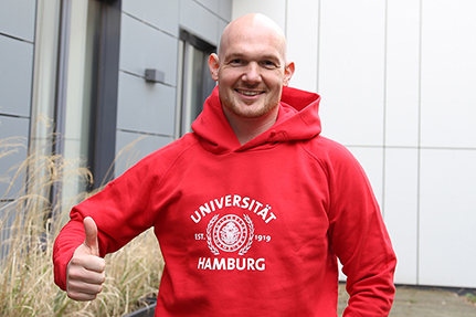 Alexander Gerst erhielt einen roten Uni-Hamburg-Hoody und schlüpfte zum Test gleich mal rein. Foto: UHH/Sukhina